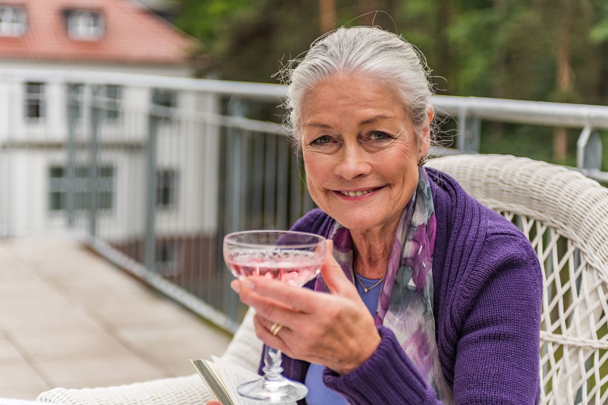 Genießen eines erfrischenden pinken Cocktails auf dem Balkon, entspannte Senioren, gemütliche Atmosphäre, Wohlfühlplatz für ältere Menschen, Hahne Wohnen, seniorengerechtes Wohnen, Lebensqualität im Alter.