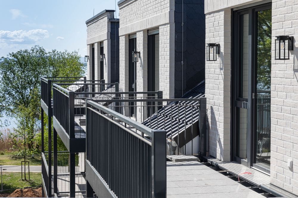 Moderner Balkon mit schwarzer Metallbrüstung und großflächigen Fenstern vor einem hellen Ziegelwohnhaus, ideal für Wohnideen und hochwertige Inneneinrichtung.