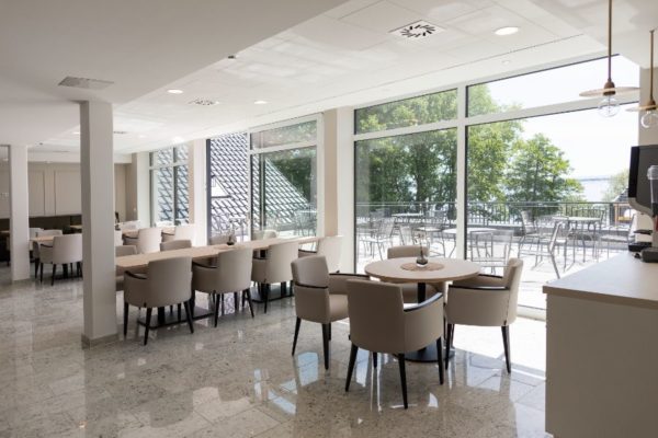 Moderne, helle Gastronomie mit großen Fenstern und Balkon, perfekt für gemütliche Cafés und Restaurants, mit eleganten Sitzmöbeln und viel Tageslicht.