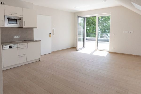 Helle, offene Wohnküche mit Zugang zum Balkon, moderne Einrichtung und große Fenster für viel Tageslicht.