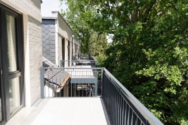 Hahne Wohnen: moderner Balkon mit Blick auf grüne Bäume, ideal für Entspannung und Outdoor-Aktivitäten.