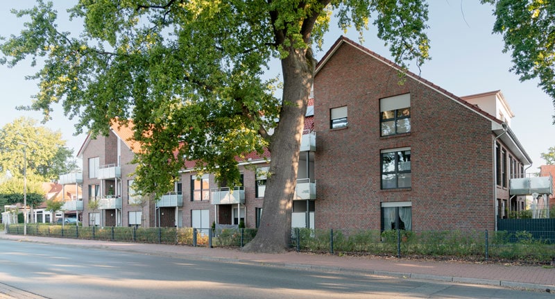 Moderne Mehrfamilienhaussiedlung mit grünen Bäumen und komfortablen Balkonen in einer ruhigen Wohngegend in Deutschland.