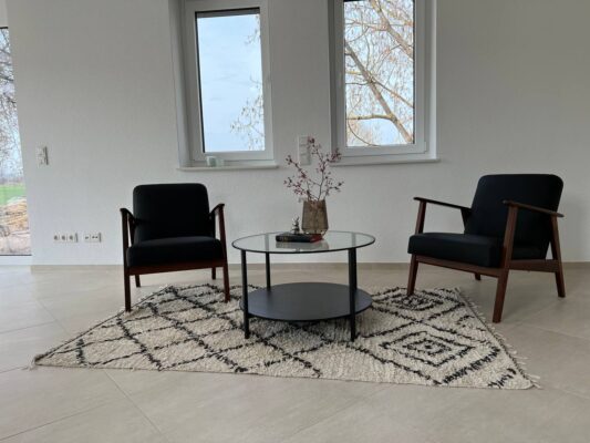 Moderner Wohnbereich mit stilvollen schwarzen Armchairs und Couchtisch auf ansprechender Teppichfläche, viel natürliches Licht, ideale Einrichtung für zeitgemäßes Wohnen.