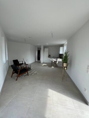 Moderner, heller Wohnzimmerbereich mit weißem Interieur, offen gestaltet mit Sitzgelegenheiten, Küchenbereich und viel natürlichem Licht, ideal für modernes Wohnen und stilvolle Inneneinrichtung.