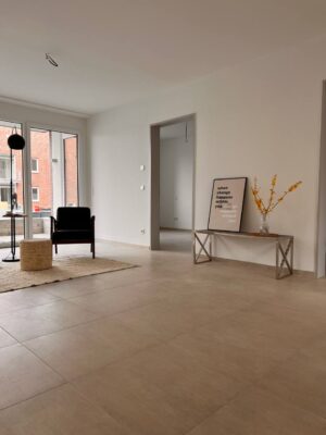 Moderner, heller Wohnbereich in einer frisch renovierten Wohnung mit großen Fenstern, minimalistische Einrichtung, Holzboden, Dekor mit Texten und Blumen, ideal für zeitgemäßes Wohnen in Deutschland.