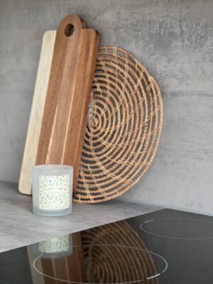 Naturholzküchenbrett, Dekorationskorb, Kerze und Glaskerze auf moderner Küchenarbeitsplatte, stilvolle Küchendekorationen für freundlich Wohnambiente.