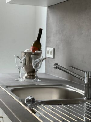Elegante Küchenspüle mit modernem Wasserhahn, stilvolle Dekoration mit Wein und Gläsern, hochwertige Küchenarbeitsplatte in zeitlosem Design, perfekt für moderne Wohnen und Küchenplanung.
