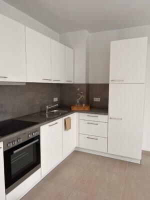 Hahne Wohnen Küche, moderne weiße Küchenschränke mit grauem Arbeitsplatten-Design, funktionale Küchenzeile mit Herd, Spüle und Stauraum, stilvolle Küchenlösung für modernes Wohnen.