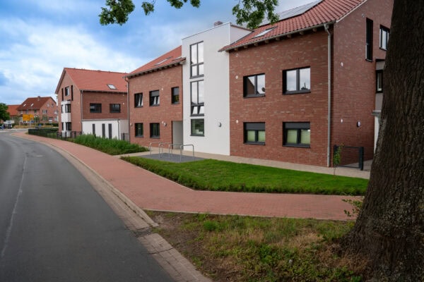 Moderne Mehrfamilienhäuser in urbaner Lage mit attraktiven Fassaden aus roten Ziegeln, großzügigen Fenstern und gepflegtem Grünbereich, ideal für wohnungsnahe Lebensqualität und Stadtentwicklung.