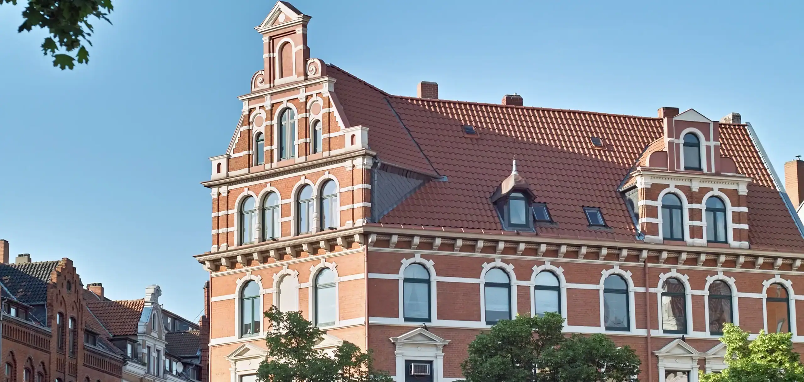 Historisches Gebäude in der Stadt mit rotem Ziegeldach und klassischen Fassadendetails, repräsentativ für hochwertige Wohn- und Einrichtungslösungen von Hahne Wohnen.